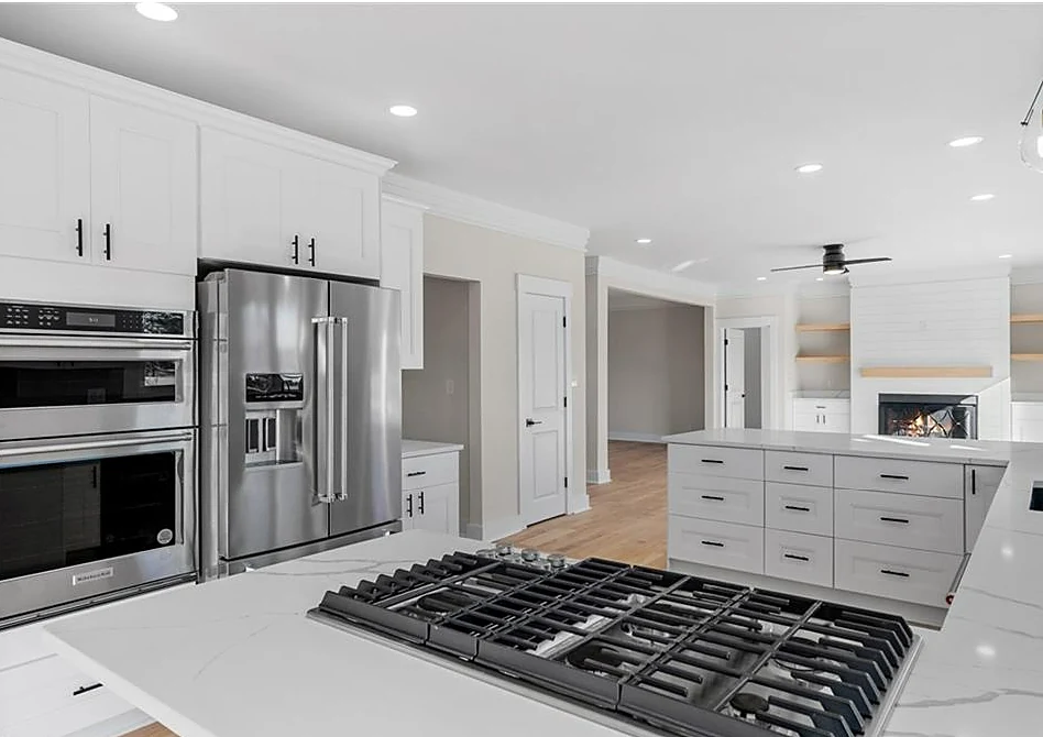 Renovated kitchen with white shaker cabinetry, stainless double wall ovens and a gas cooktop set in a quartz island
